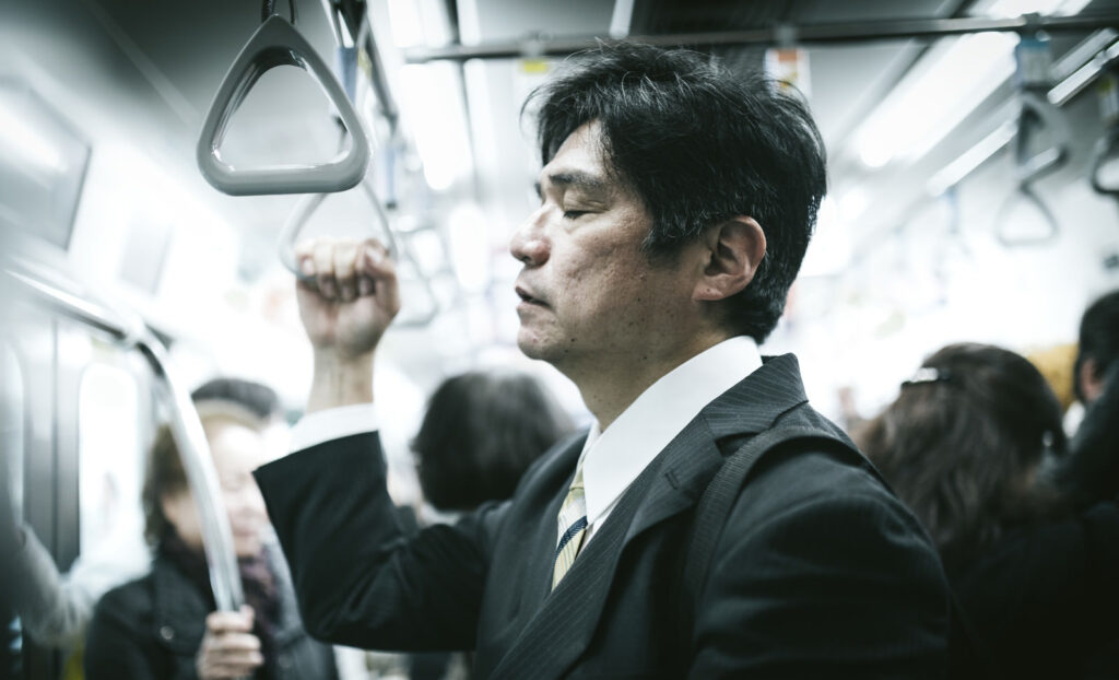 電車の中で疲労して寝ている男性